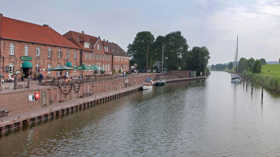 A canal with boats, a brick building with green awnings, and a grassy embankment.