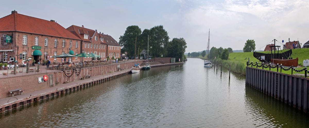 A canal with boats, a brick building with green awnings, and a grassy embankment.