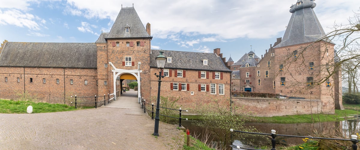 A historic brick building with a tower and a canal in the foreground.