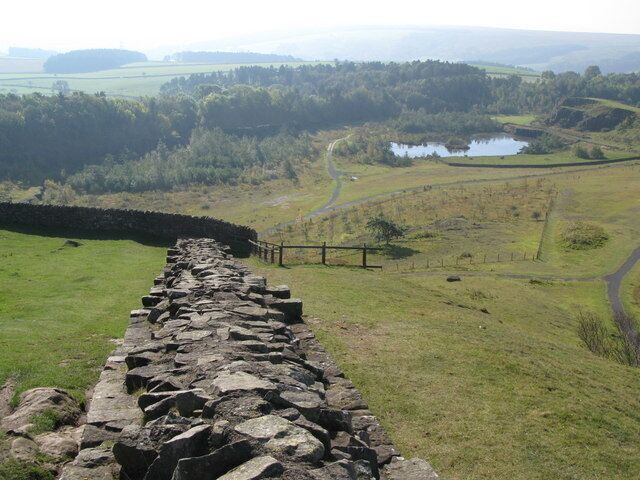 A stone wall leading to a pond surrounded by fields and trees.