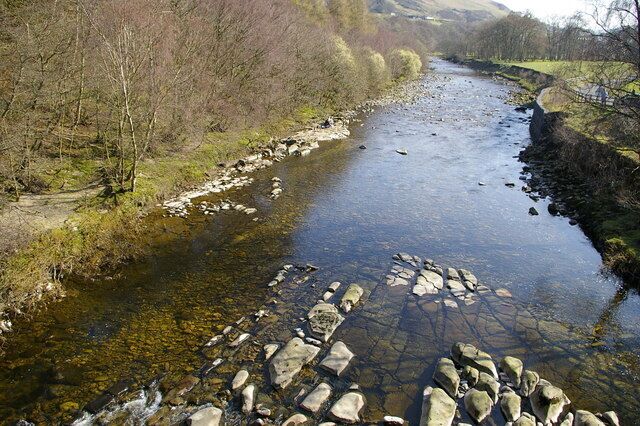 A river with clear water, surrounded by rocky banks and sparse vegetation.