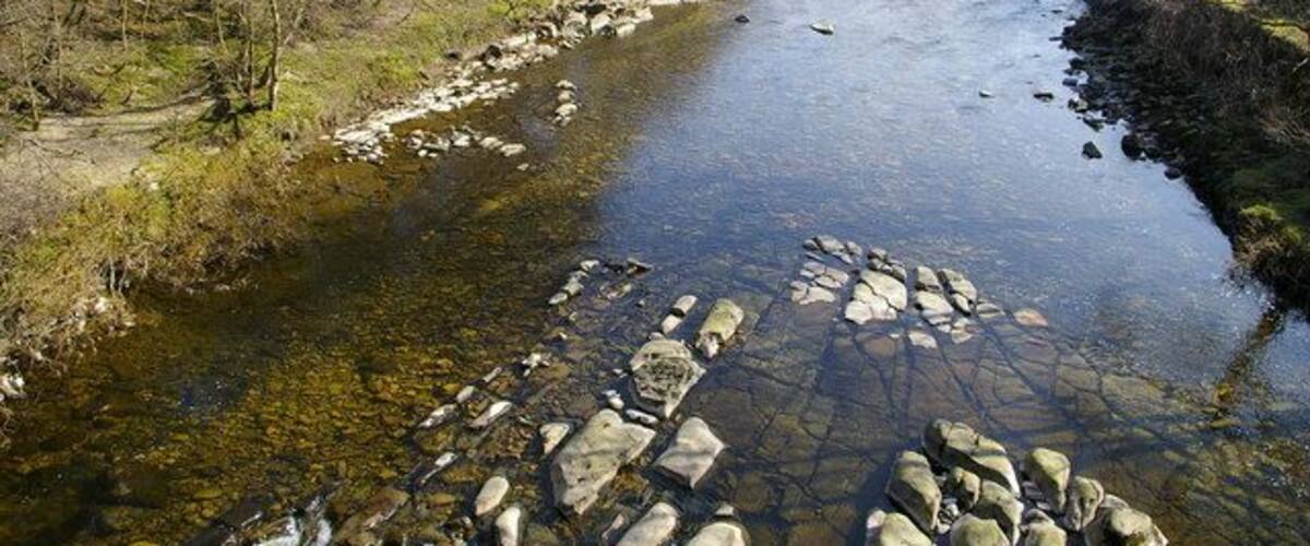 A river with clear water, surrounded by rocky banks and sparse vegetation.