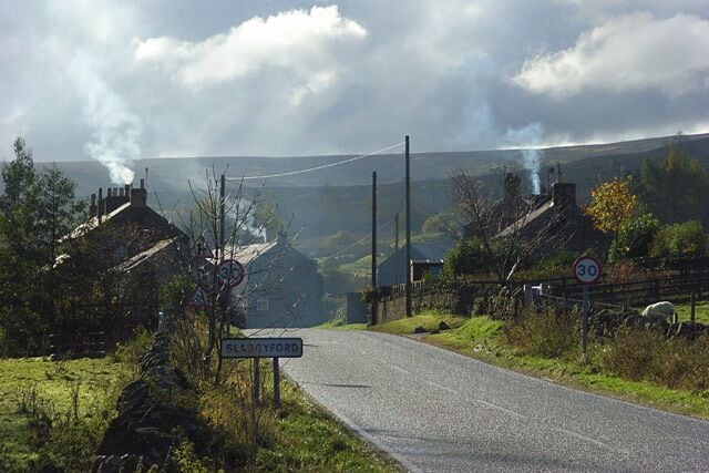A rural road with a speed limit sign, a sign for Blagoevgrad, and smoke in the distance.