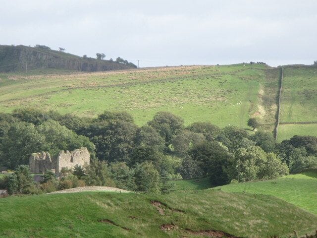 A rural landscape with rolling hills, a stone building, and a fence.