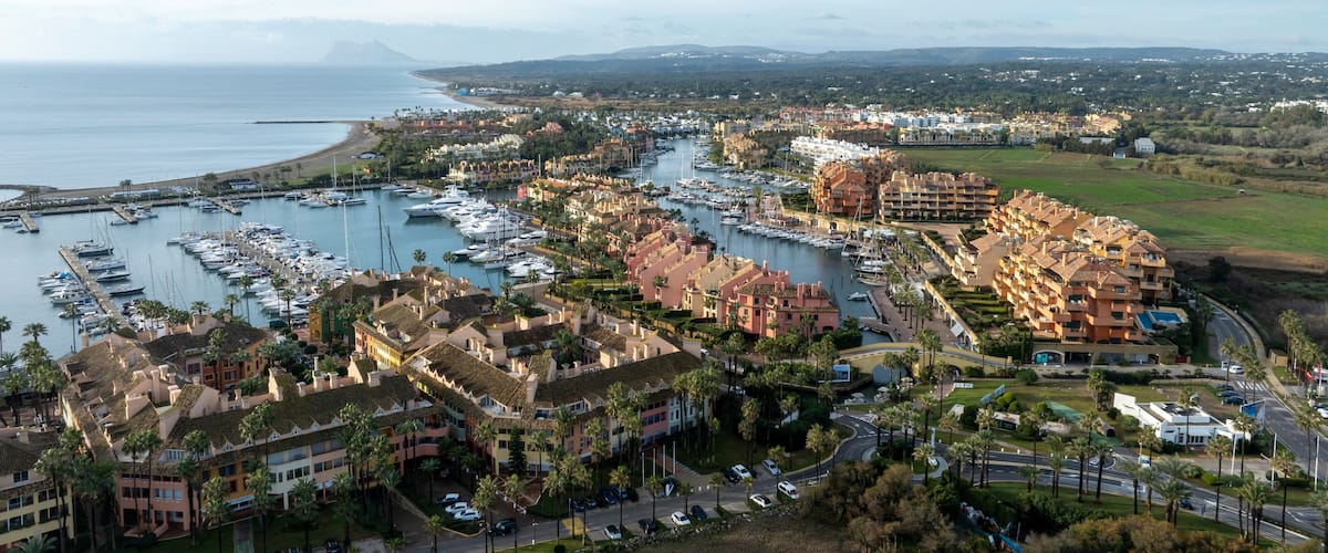 A coastal marina with numerous boats, a beach, and residential buildings.
