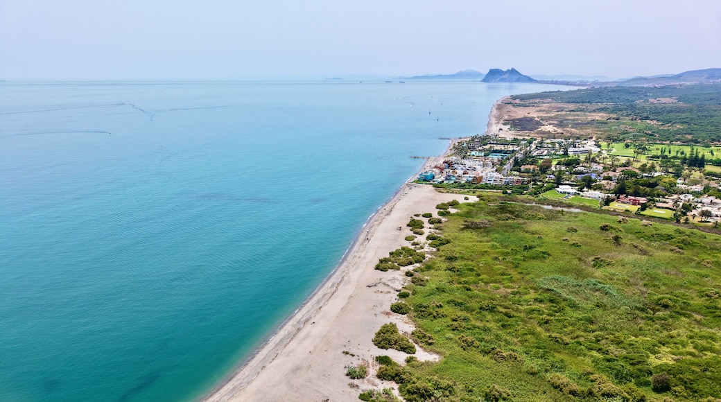 A coastal landscape with a sandy beach, a small town, and a mountain in the distance.