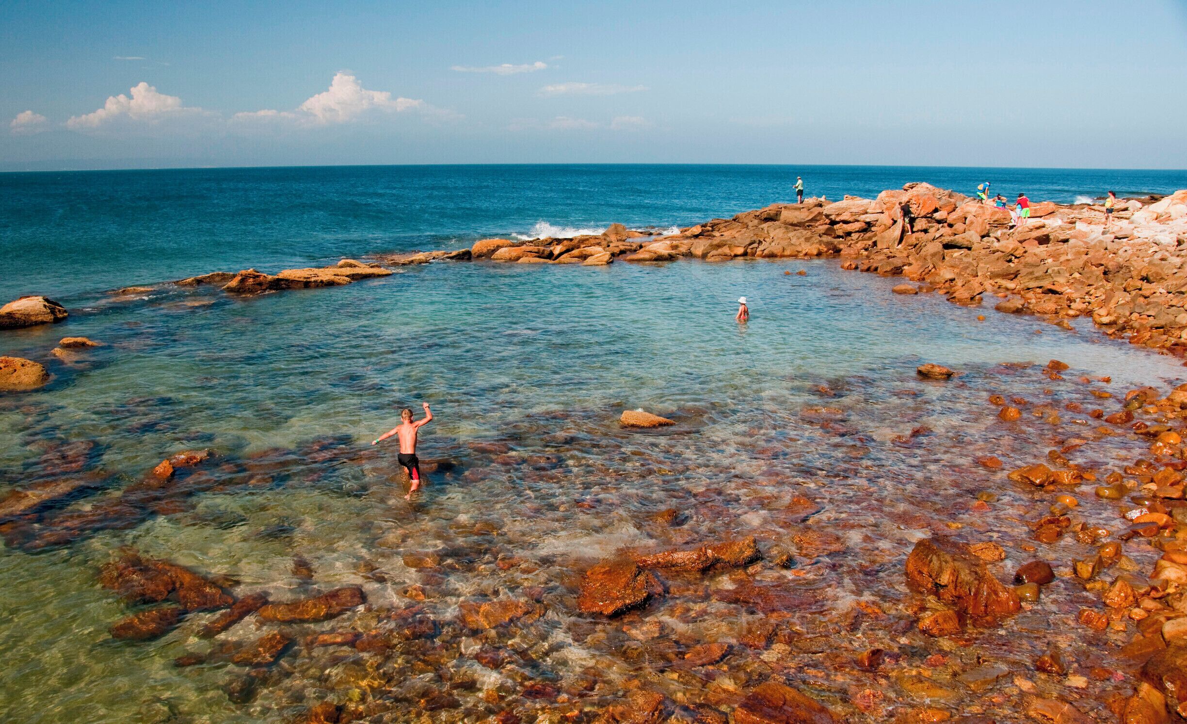 A rocky shoreline with clear water and people swimming.