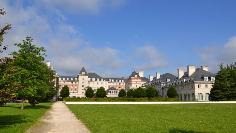 A large, historic building with multiple towers and a well-maintained lawn in front.