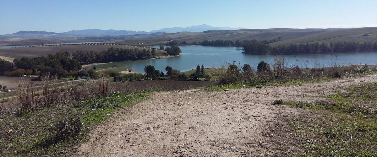 A lake surrounded by hills and sparse vegetation.