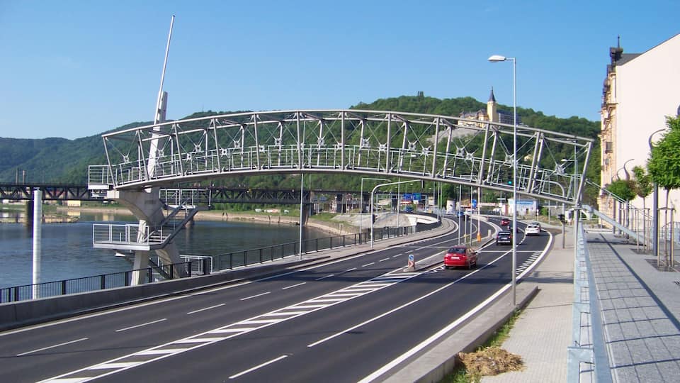 A modern bridge over a river, a road with cars, and a cityscape with buildings.