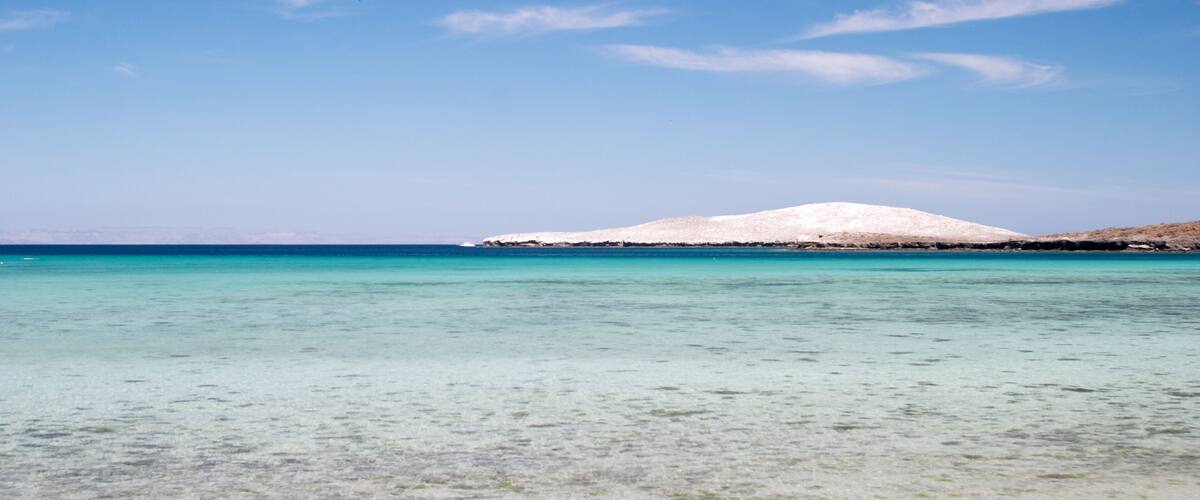 A clear turquoise sea with a snow-capped island in the distance.