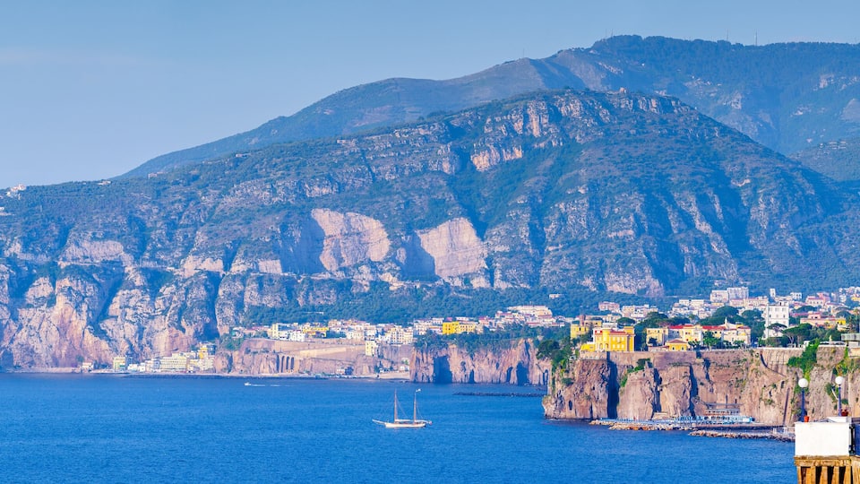 A coastal town with buildings on a cliffside, a large rock formation, and the sea.