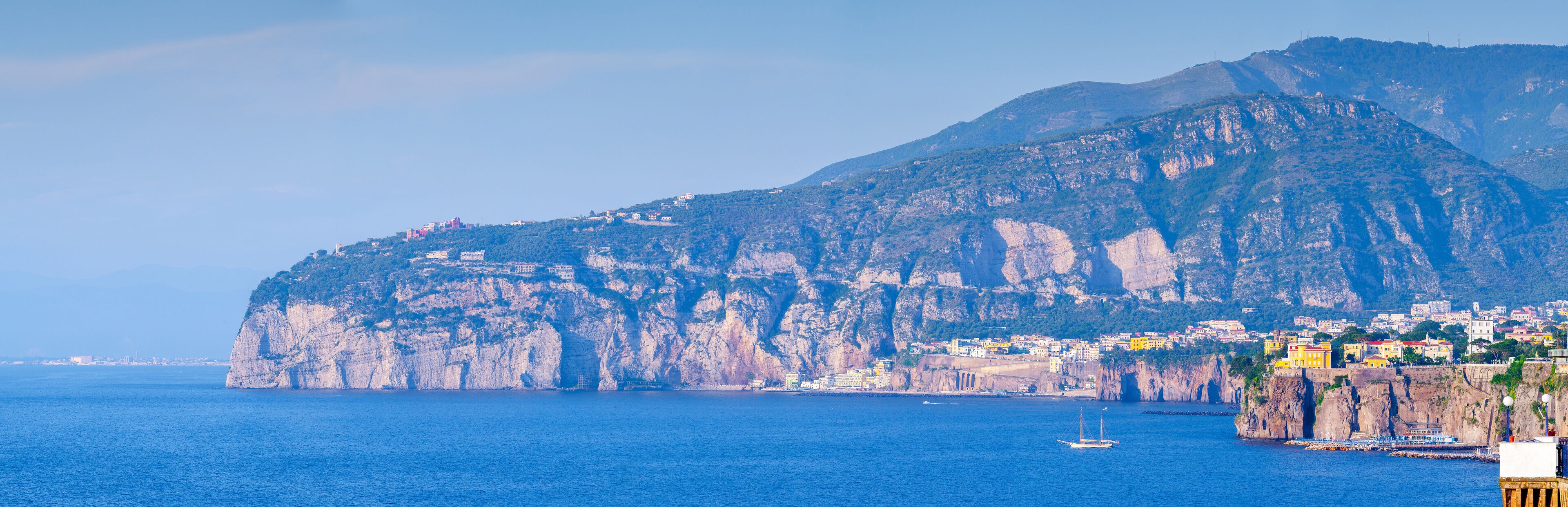 A coastal town with buildings on a cliffside, a large rock formation, and the sea.