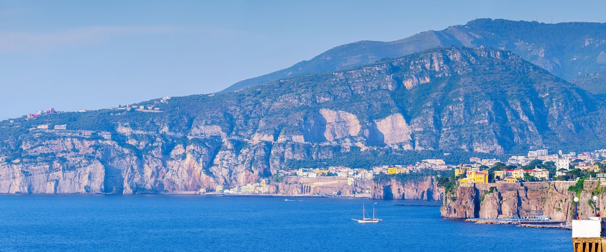 A coastal town with buildings on a cliffside, a large rock formation, and the sea.