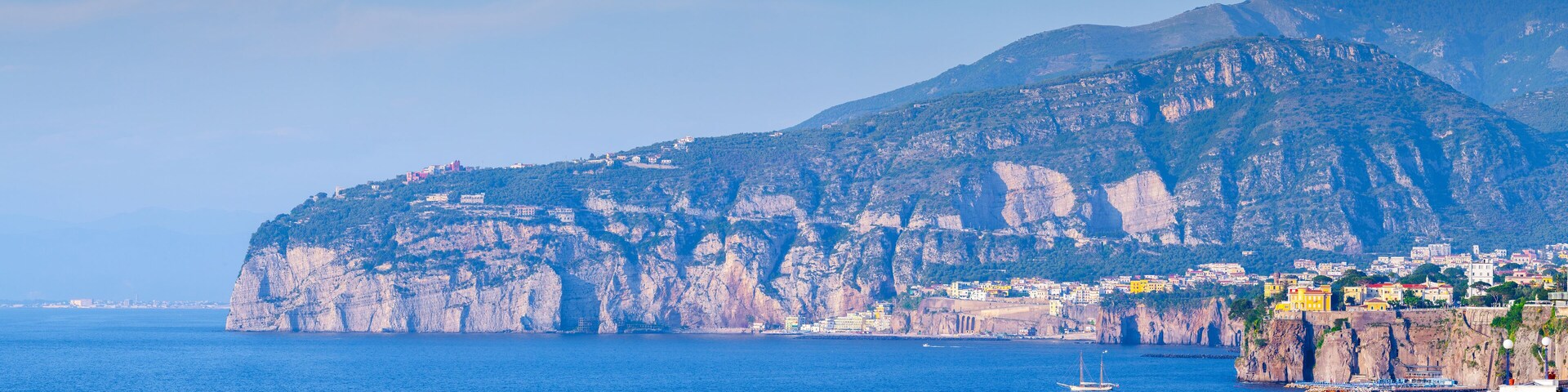 A coastal town with buildings on a cliffside, a large rock formation, and the sea.