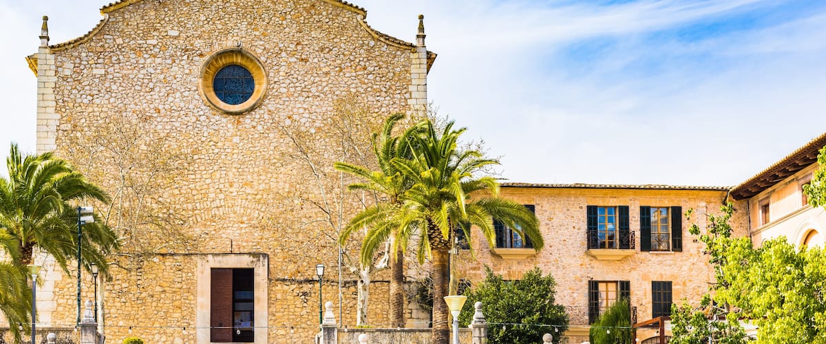 A stone church with a bell tower, palm trees, and a staircase leading to the entrance.