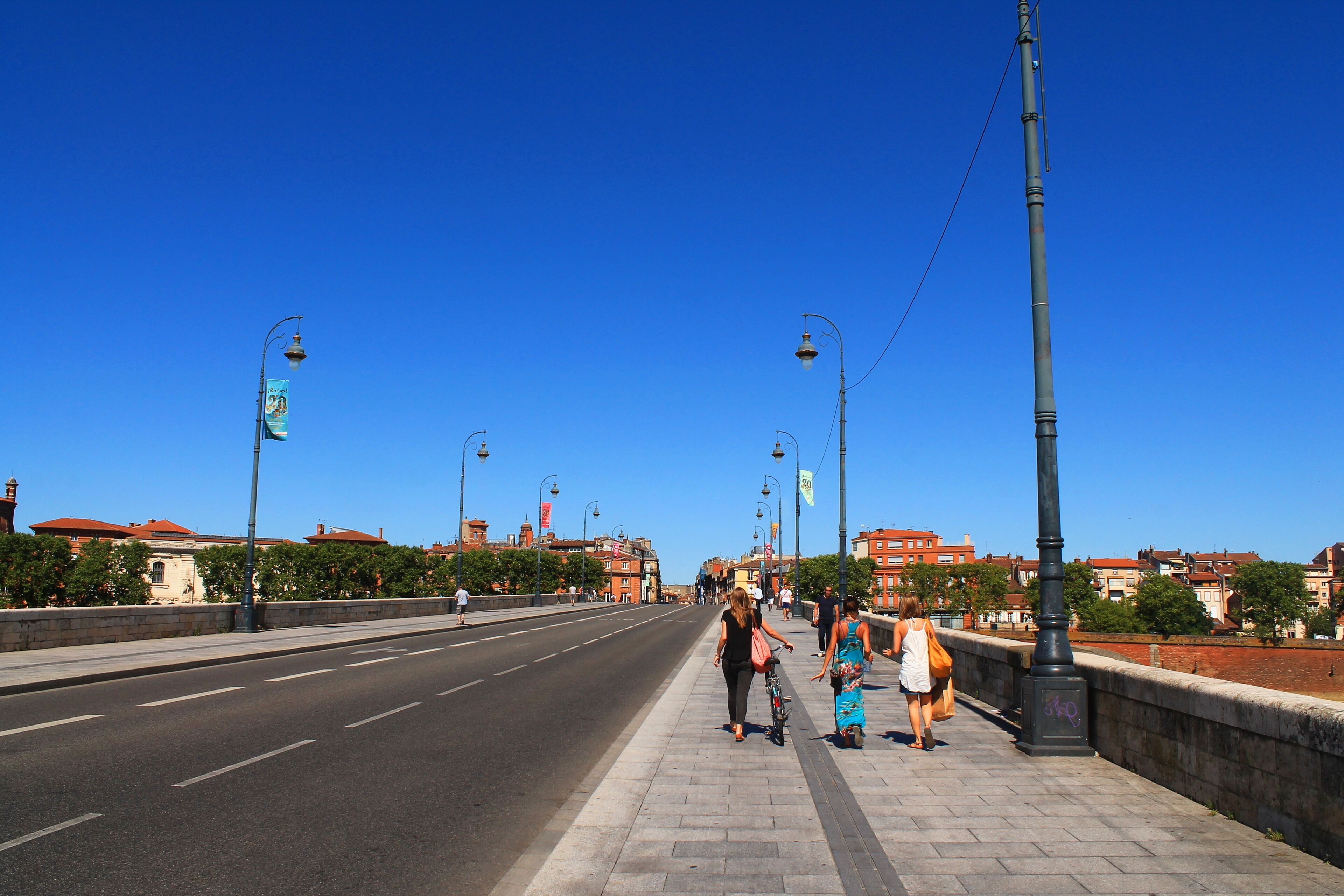 Un cielo azul despejado, una carretera ancha y una acera con gente caminando y un ciclista.