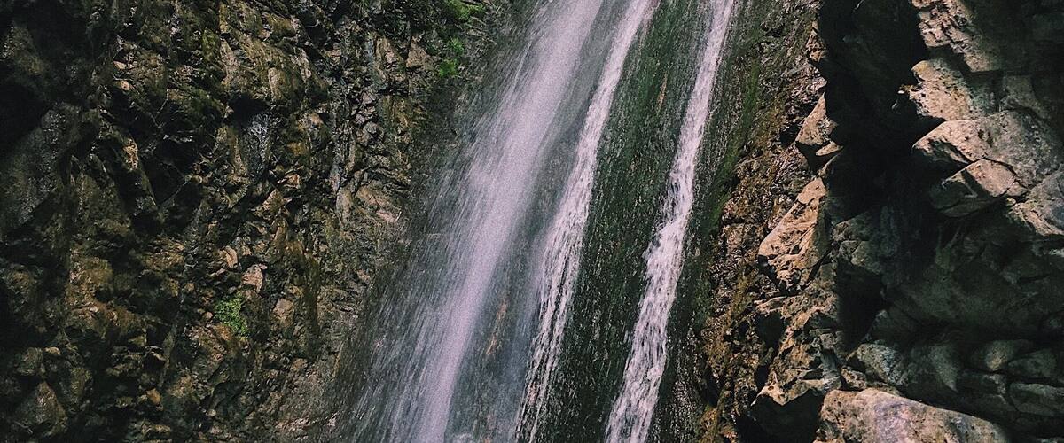 A waterfall cascading down a rocky cliff surrounded by lush greenery.