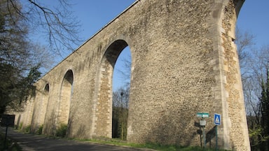 Un viaducto de piedra con múltiples arcos, una señal de tráfico que indica un paso de peatones, y un cartel que dice 'Rue de la Casale'.