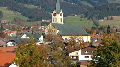 A church with a tall steeple and a clock tower, surrounded by houses and autumn-colored trees.