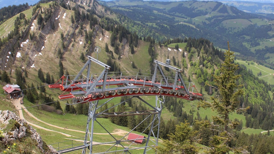 A cable car system in a mountainous area with green valleys and forested hills.