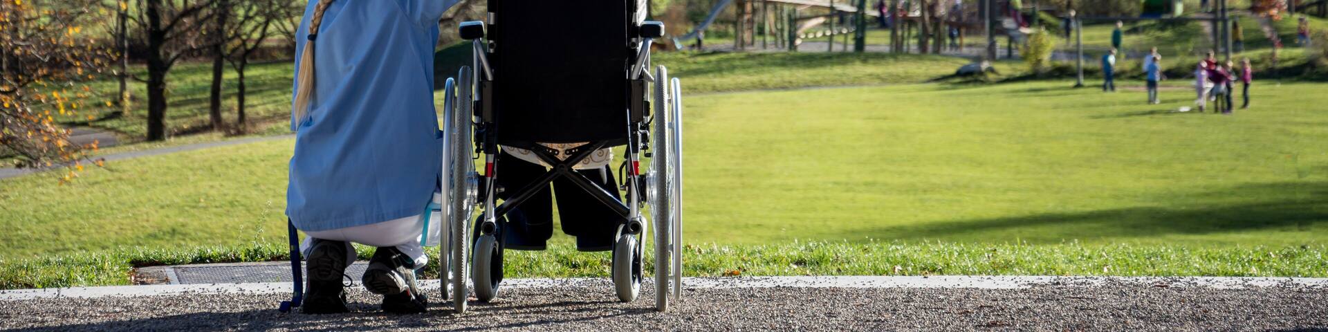 Seniorin im Rollstuhl blickt mit ihrer Pflegerin in die Allgäuer Berge
