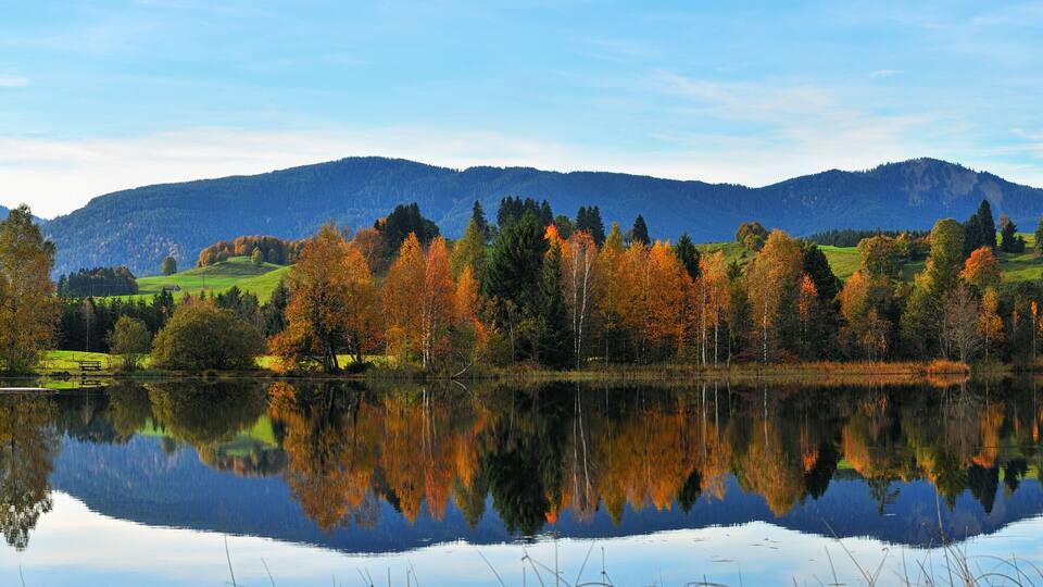 A calm lake reflecting autumn trees and mountains.