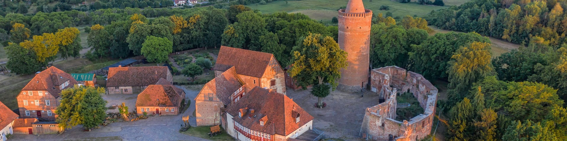 An aerial view of a historic village with a prominent tower, surrounded by lush greenery and traditional buildings.