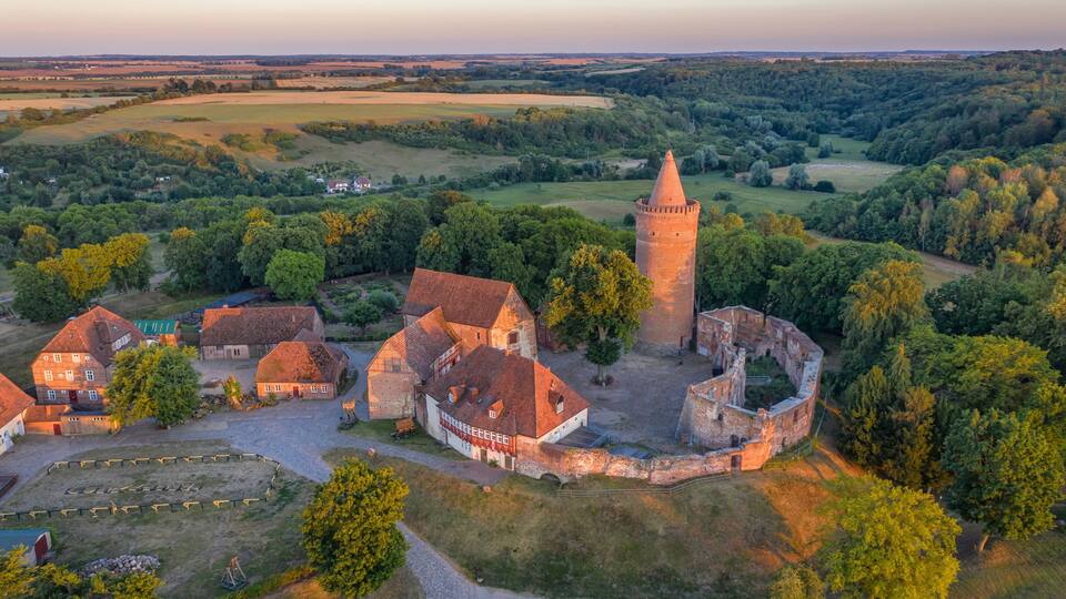 An aerial view of a historic village with a prominent tower, surrounded by lush greenery and traditional buildings.