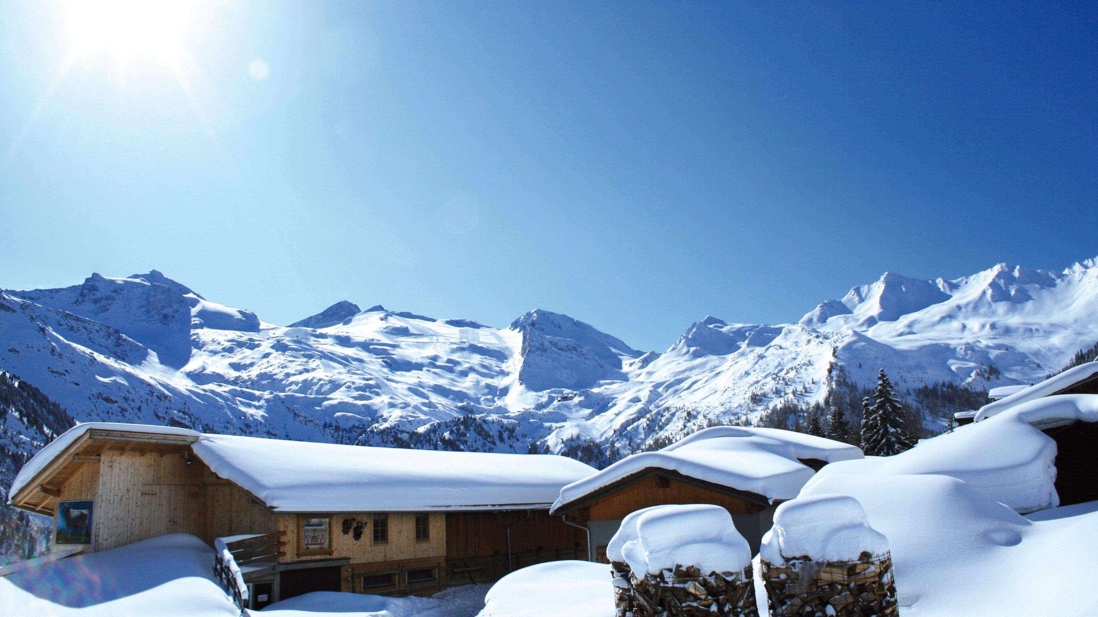 A snow-covered mountain landscape with wooden cabins and a clear blue sky.