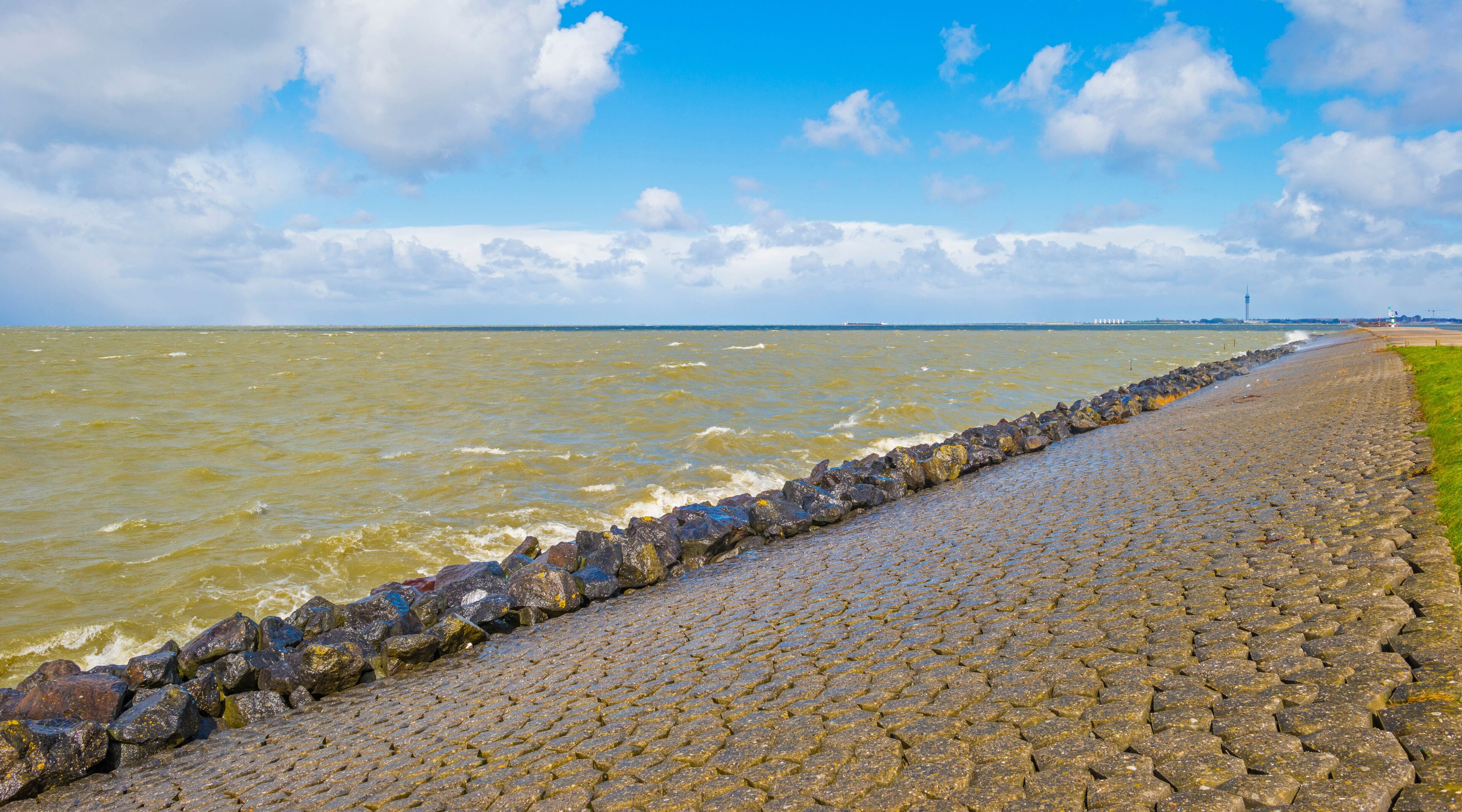 Dike of basalt stones defying a stormy lake below a blue sky and white gray clouds in spring, Almere, Flevoland, The Netherlands, April 5, 2021