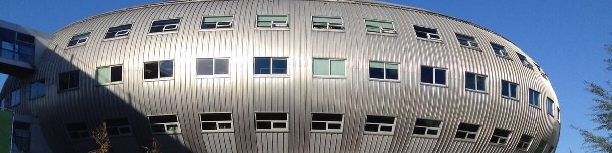 A modern, curved building with a metallic exterior and multiple windows.