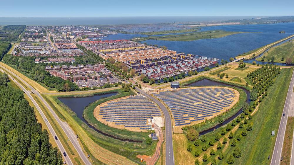 An aerial view of a coastal city with a large marina, a highway, and a solar farm.