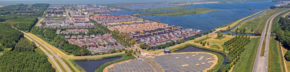 An aerial view of a coastal city with a large marina, a highway, and a solar farm.