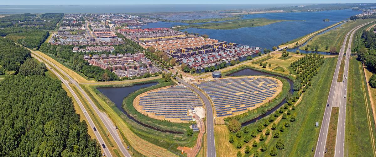 An aerial view of a coastal city with a large marina, a highway, and a solar farm.