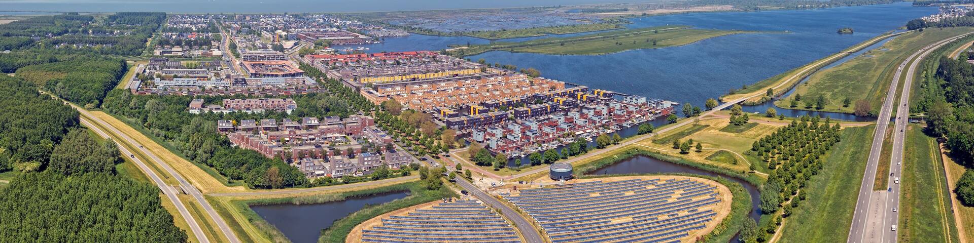 An aerial view of a coastal city with a large marina, a highway, and a solar farm.