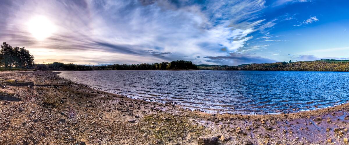 A lake with a rocky shoreline and trees in the background.
