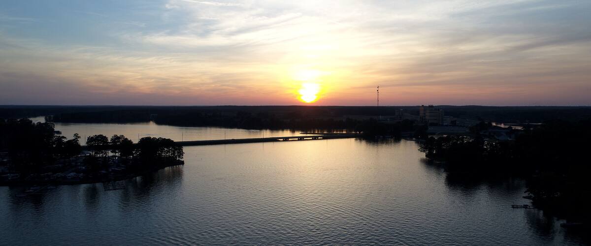 A sunset over a calm river with a bridge and distant buildings.