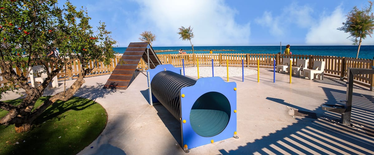 A playground with a slide, a tunnel, and a beach in the background.