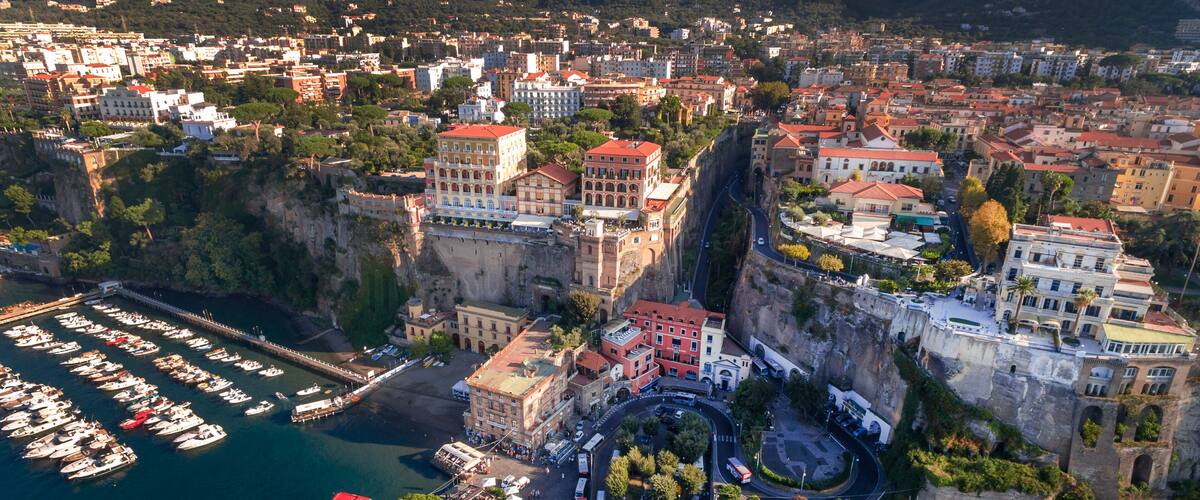 A coastal town with a marina, historic buildings, and a cliff overlooking the sea.