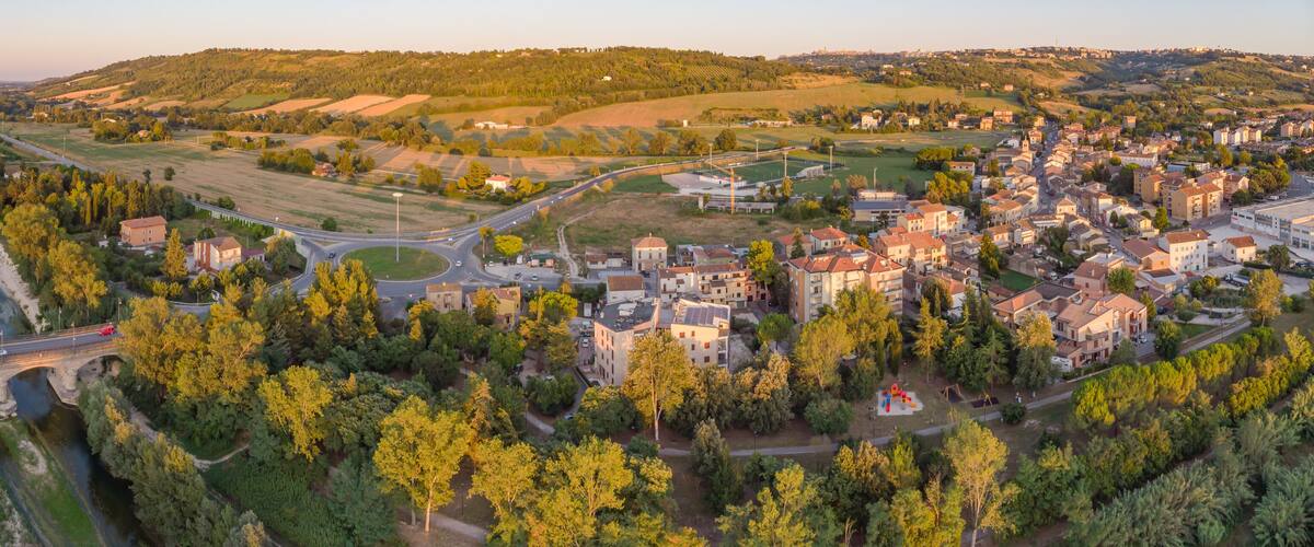 A town with a bridge over a river, surrounded by green fields and hills.