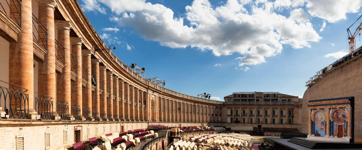 A grand architectural structure with a curved facade, large columns, and a clear blue sky with scattered clouds.