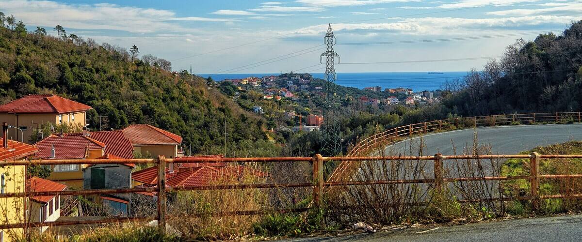 A coastal town with red-roofed houses, a power line tower, and a clear blue sky.
