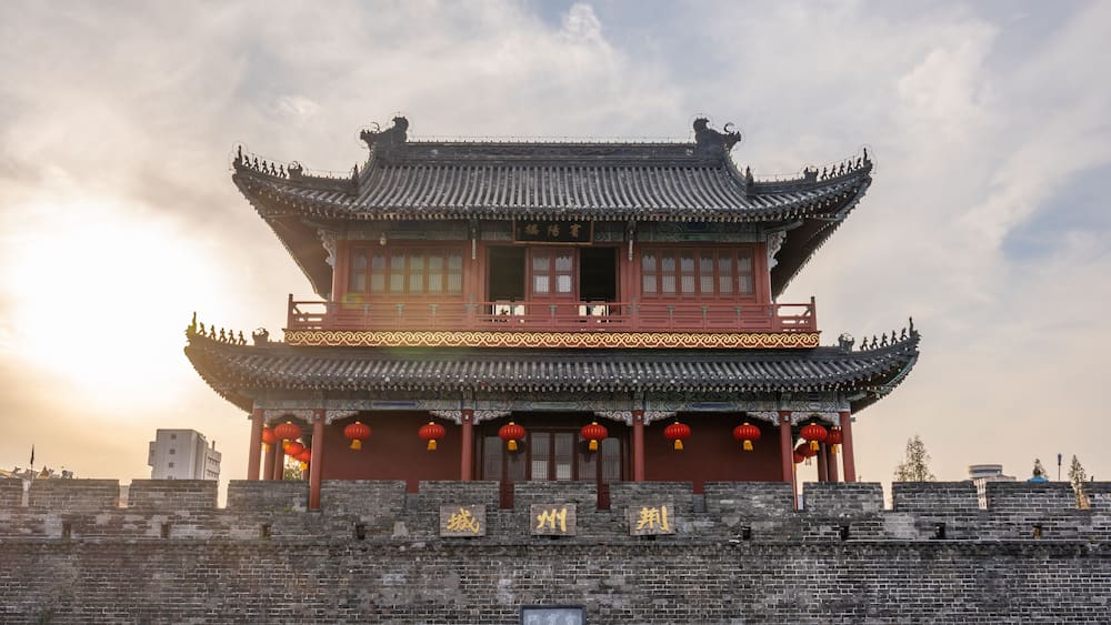 A traditional Chinese building with ornate architecture, a red roof, and a stone wall in the foreground.