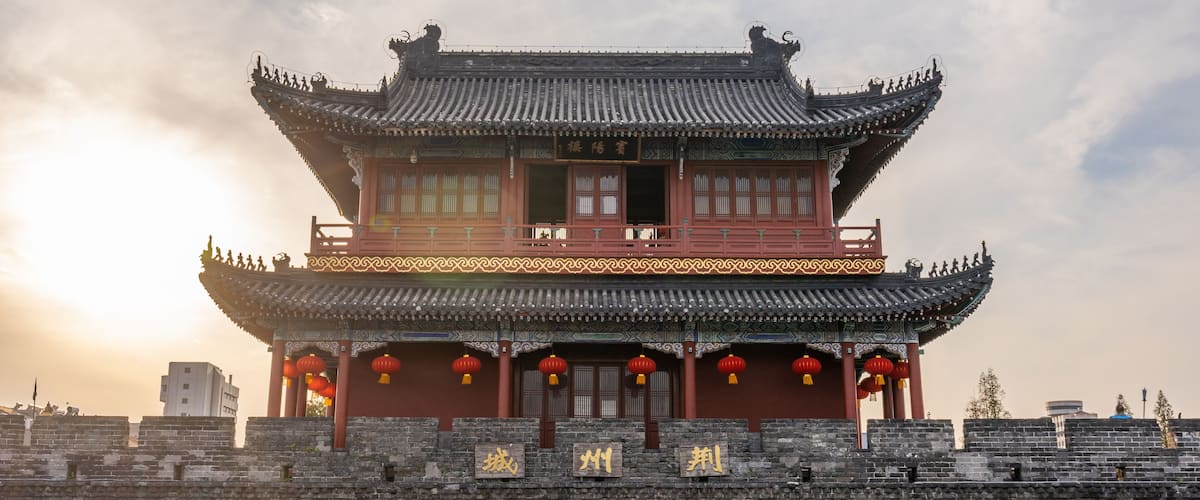 Un edificio chino tradicional con arquitectura ornamentada, techo rojo y un muro de piedra en primer plano.