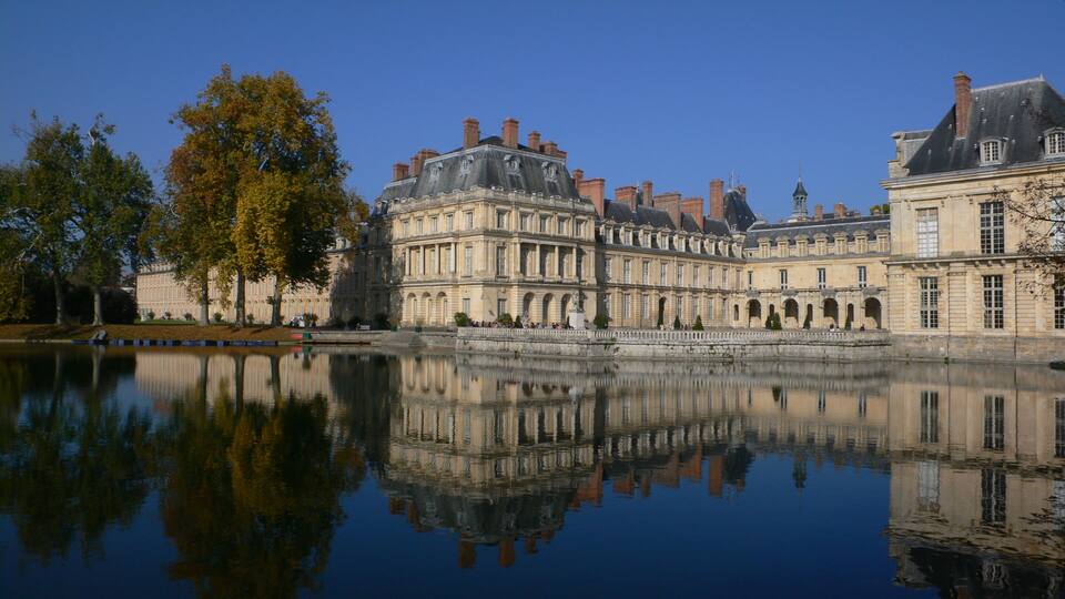 A historic building with a reflection in the water, surrounded by trees.