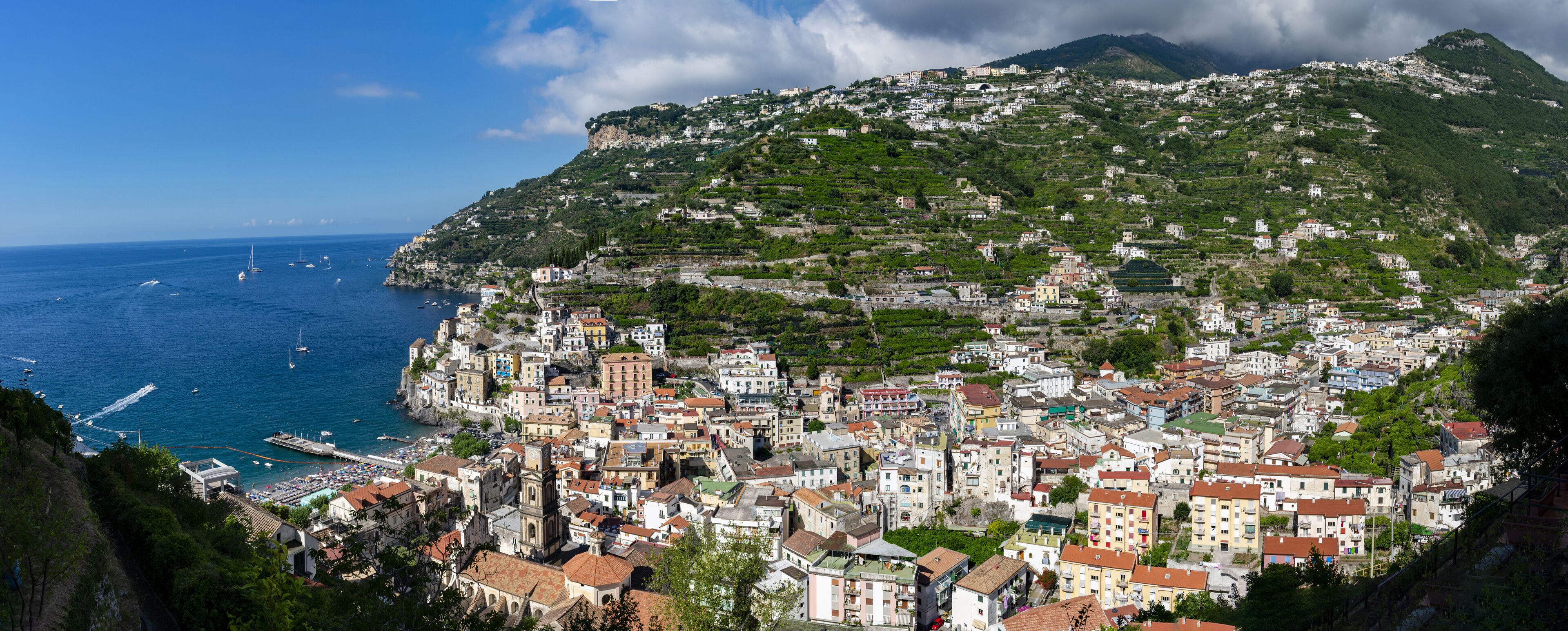 A coastal town with terraced vineyards, a harbor with boats, and buildings on a hillside.