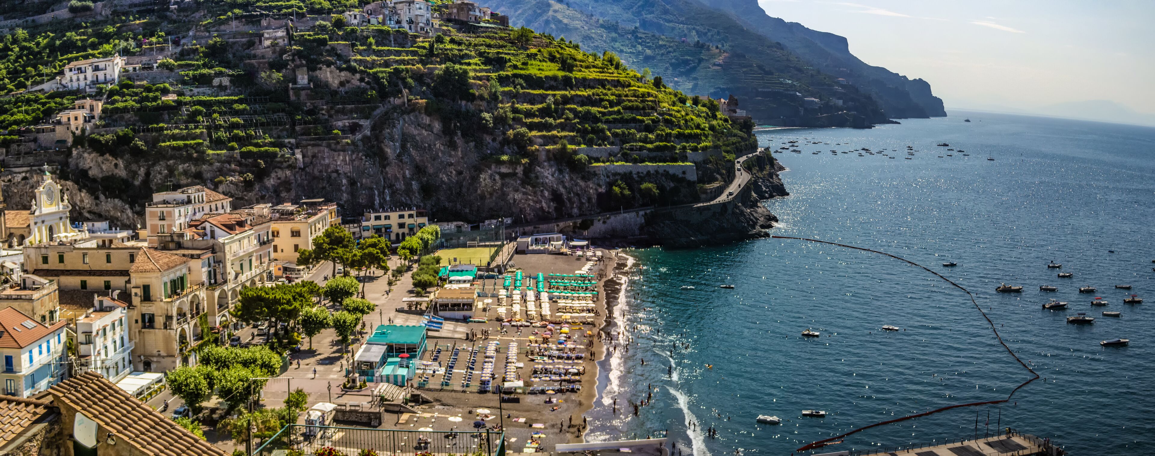 A coastal town with terraced vineyards, a beach, and boats in the water.