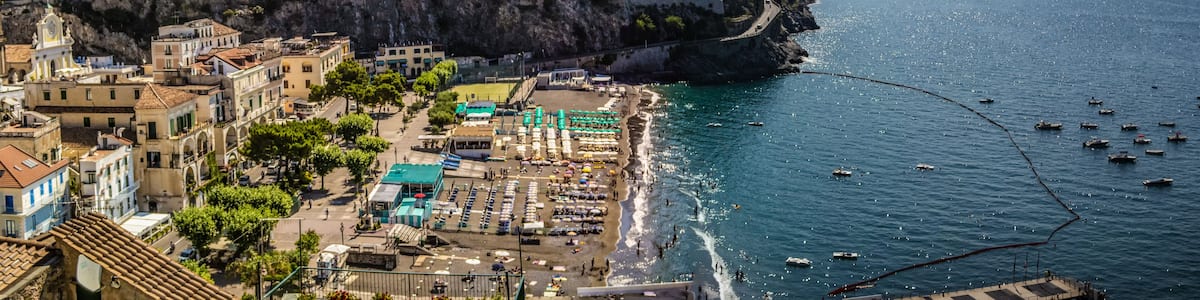 A coastal town with terraced vineyards, a beach, and boats in the water.