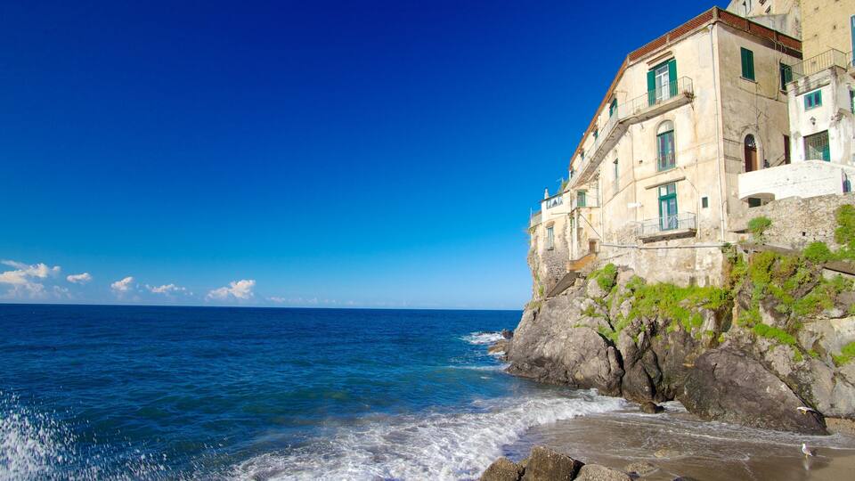 A coastal building with a stone facade and green shutters, overlooking the sea.